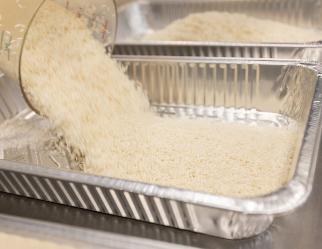 Spanish rice being seasoned and mixed in large container