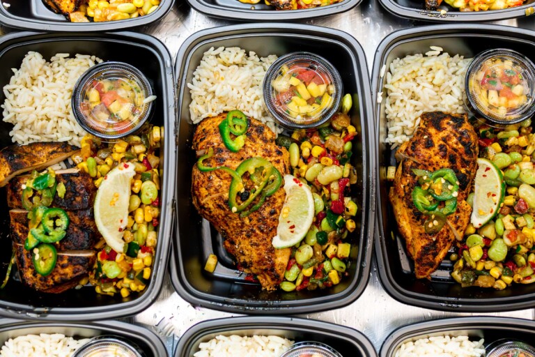 Culinary team assembling Cajun chicken meal prep in portioned trays.