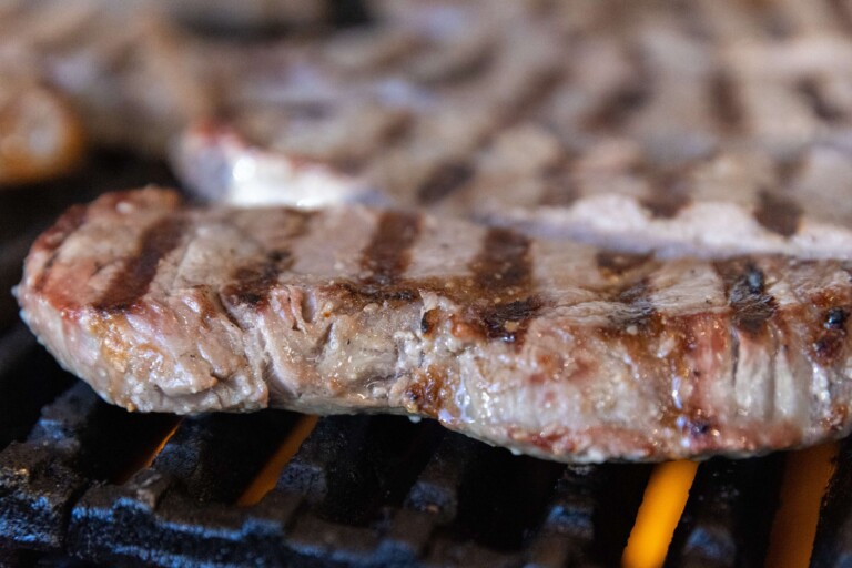 Chicken breast sizzling on commercial flat-top grill at meal prep services kitchen.