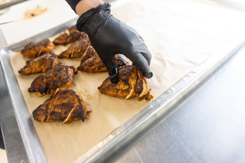 Chicken breast sizzling on commercial flat-top grill at meal prep services kitchen