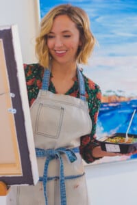 Creative woman painting at home while holding a Meal Prep Sunday meal, enjoying free time and healthy eating