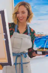 Creative woman painting at home while holding a Meal Prep Sunday meal, enjoying free time and healthy eating