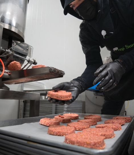 Meal Prep Sunday kitchen team member placing freshly formed raw patties from a forming machine onto a parchment-lined tray